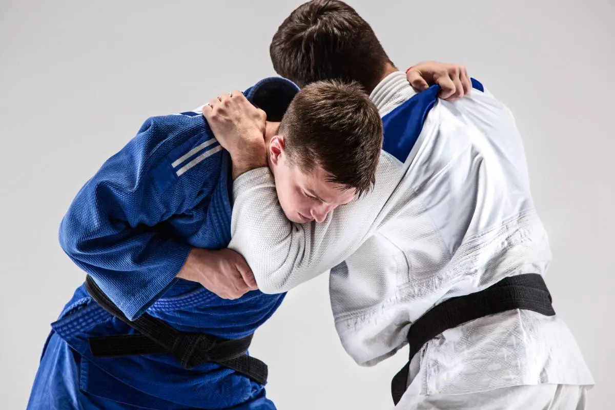 Two men in blue and white gi uniforms engaged in a close-contact grappling or throwing technique.