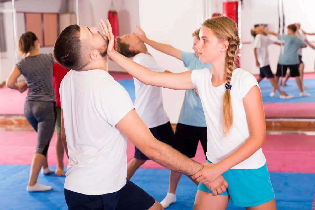 A young girl practicing a palm strike to the chin of a male instructor during a youth self-defense class.