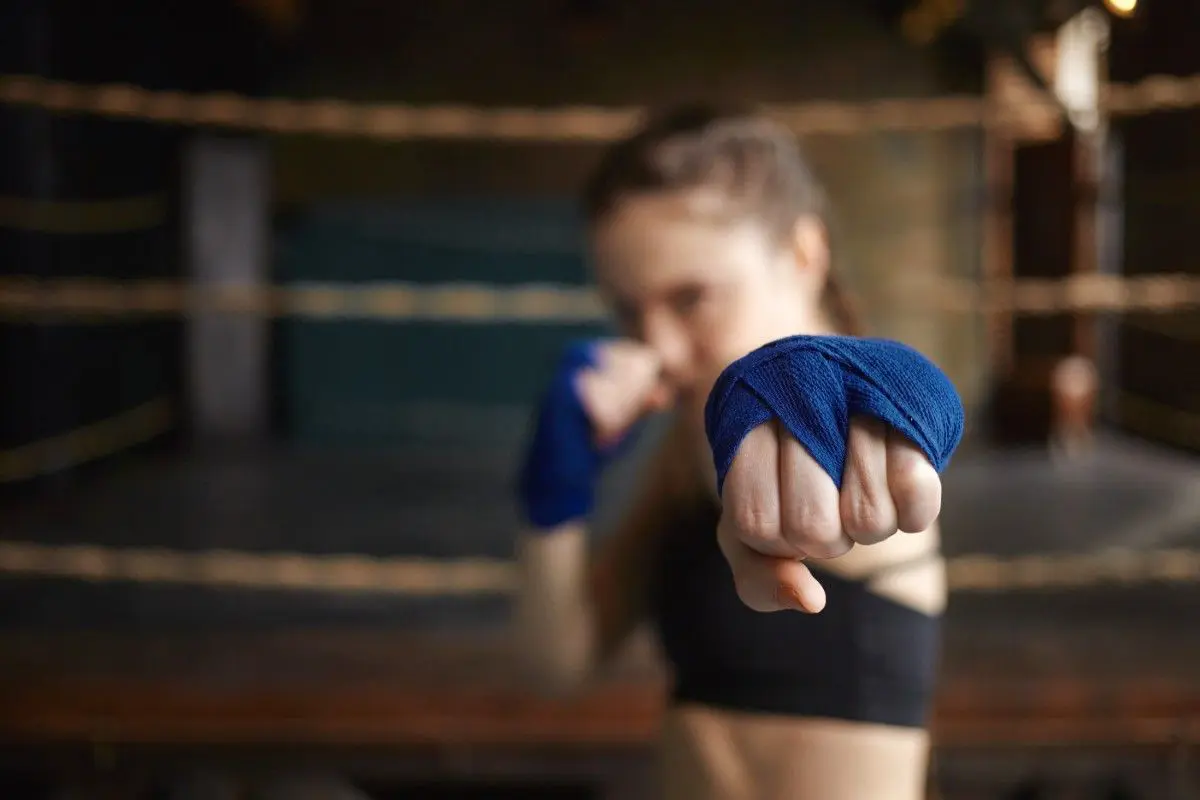 Close-up focus on a woman&rsquo;s clenched fist wrapped in blue boxing tape, positioned in a fighting stance.