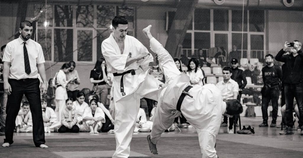 A black and white photo of a martial arts sparring match with an athlete landing a high kick, demonstrating advanced techniques learned through a kenpo karate belt system explained.