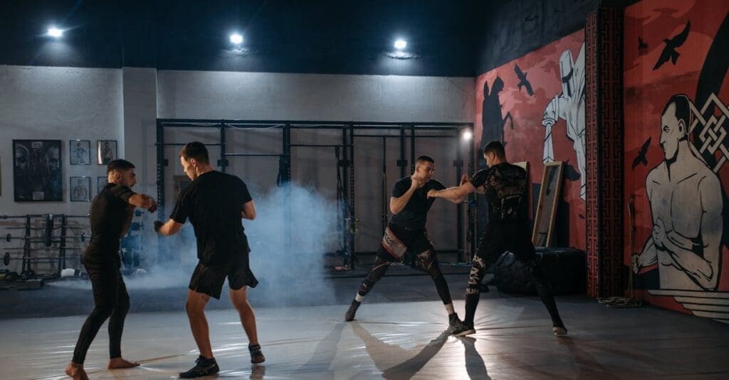 Multiple martial artists sparring under bright lights in a modern combat sports gym, showing the disciplined environment highlighted in a teen self defense guide.