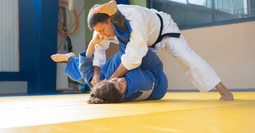 A teenage martial artist in a blue gi executing a dynamic throwing technique on an opponent during a training session, serving as a visual example for a teen self defense guide.
