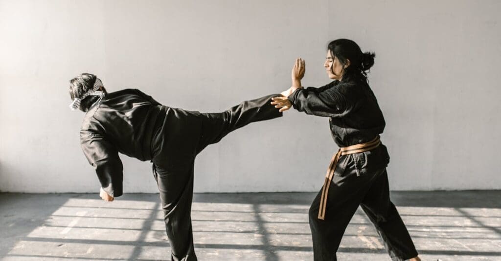 Two martial artists practicing a defensive block against a high side kick in a bright training room, ideal for illustrating martial arts techniques in a teen self defense guide.