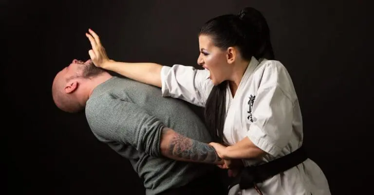 A woman in a martial arts uniform executing a powerful palm strike to an attacker's face, demonstrating practical close-combat strikes for a teen self defense guide.